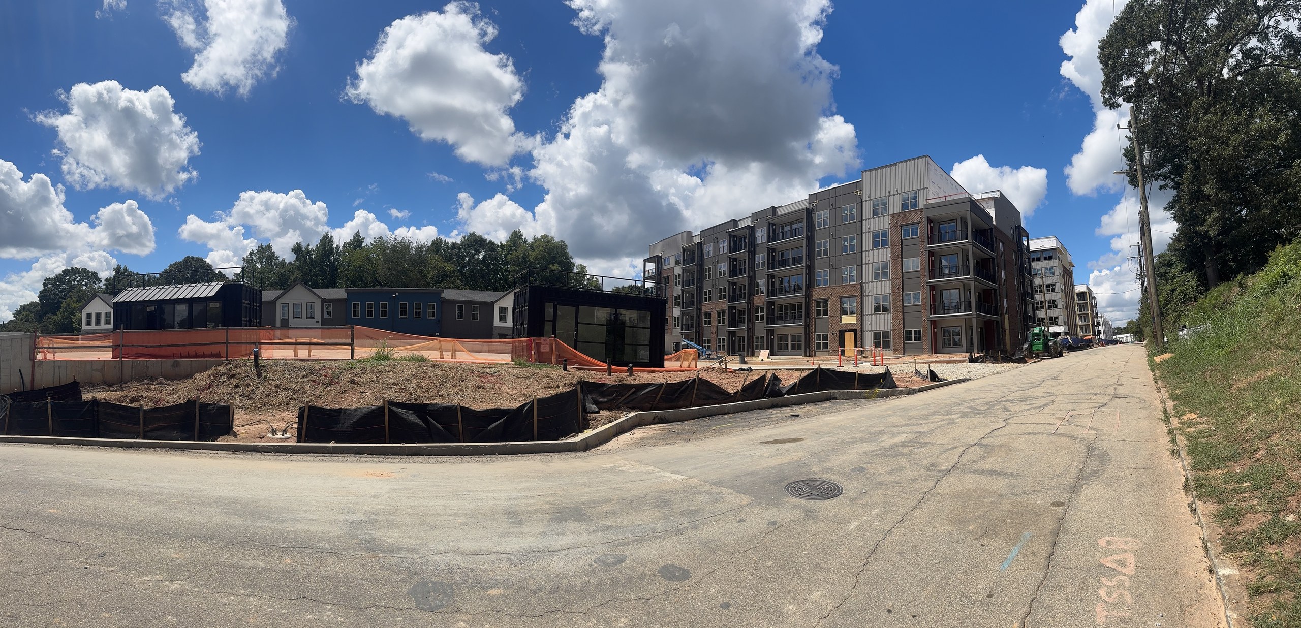 Panoramic street view of Woodrow House, with the apartment building, low-rise structures and active site work beneath a blue sky.